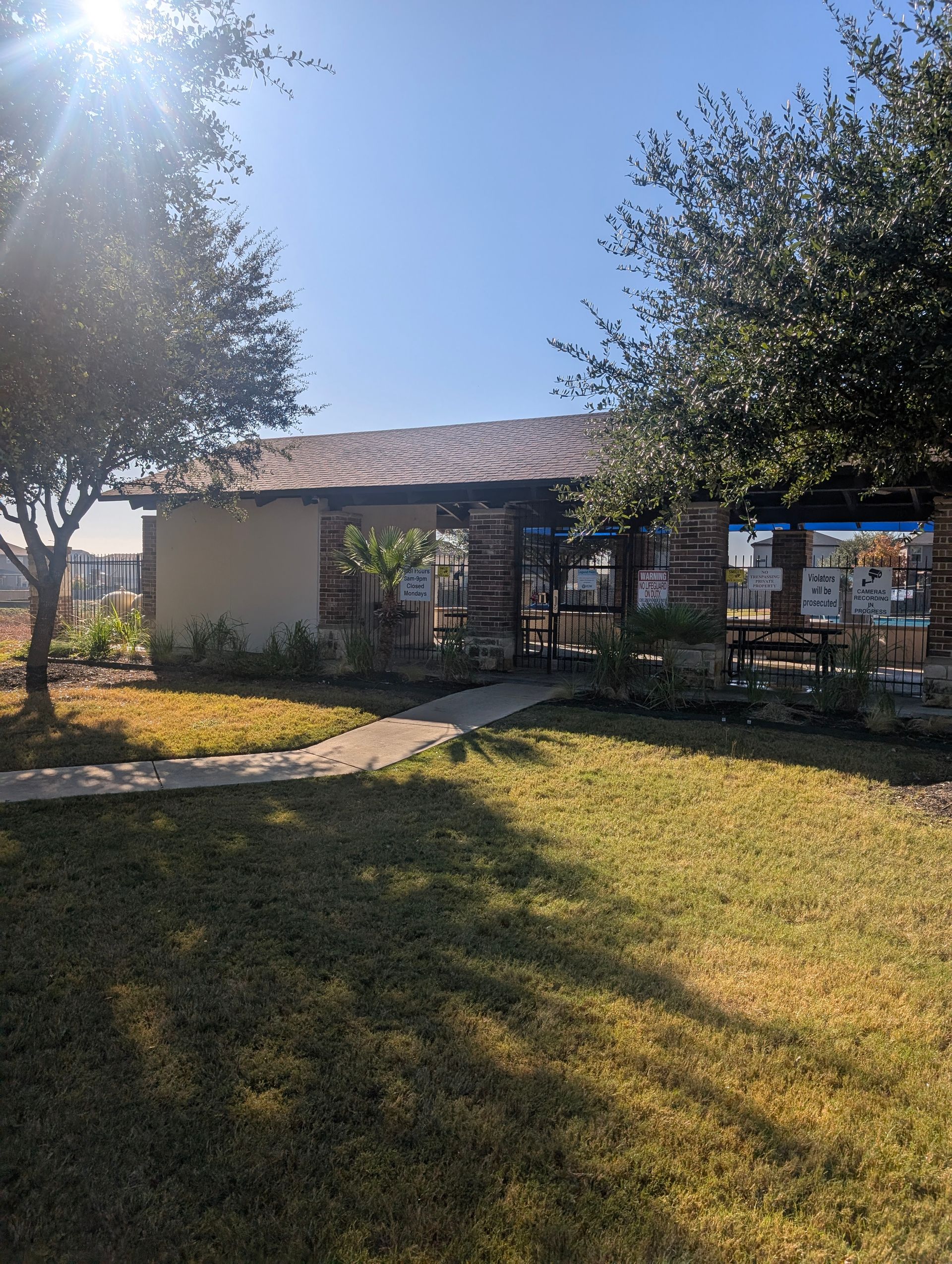 A small building with a stone facade, a brown roof, and a walkway; surrounded by green grass and trees under a sunny sky.