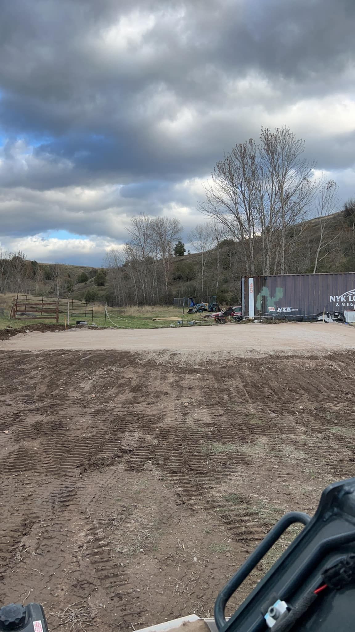 A view of a dirt field from a vehicle with a cloudy sky in the background.
