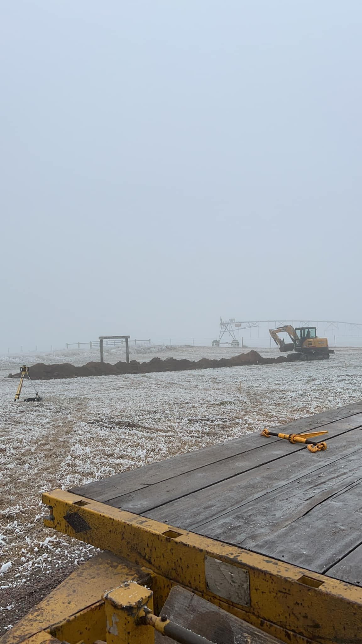 A yellow bulldozer is sitting on top of a wooden dock next to a body of water.