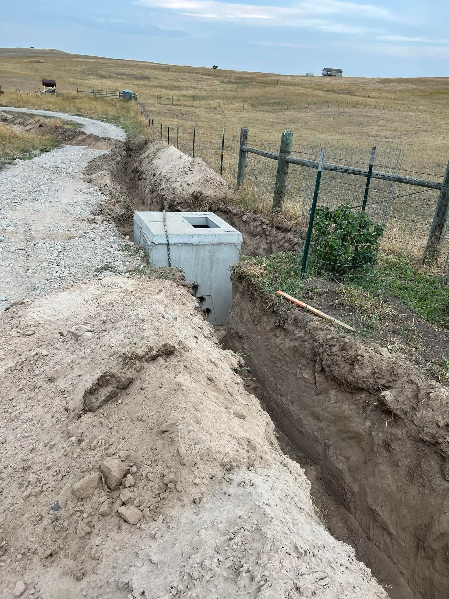 A concrete box is sitting in the middle of a dirt field next to a dirt road.