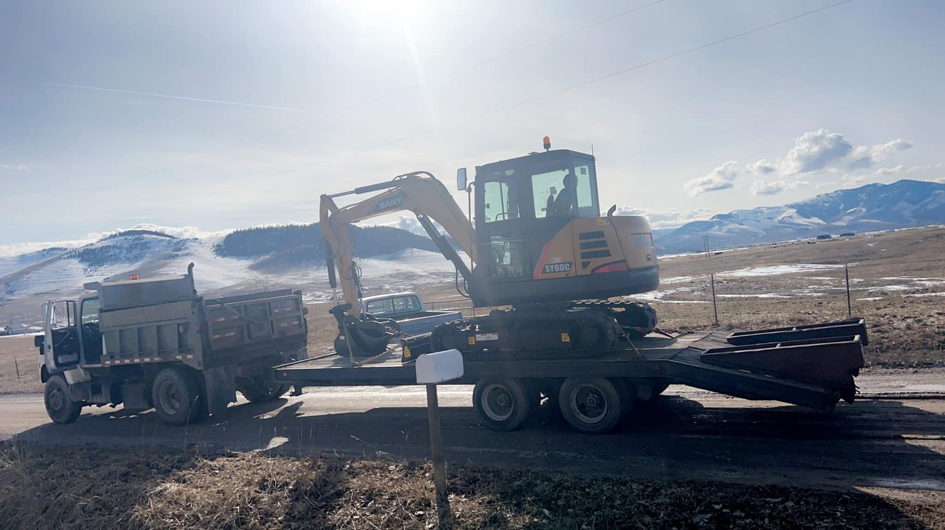 An excavator is being towed by a dump truck on a dirt road.