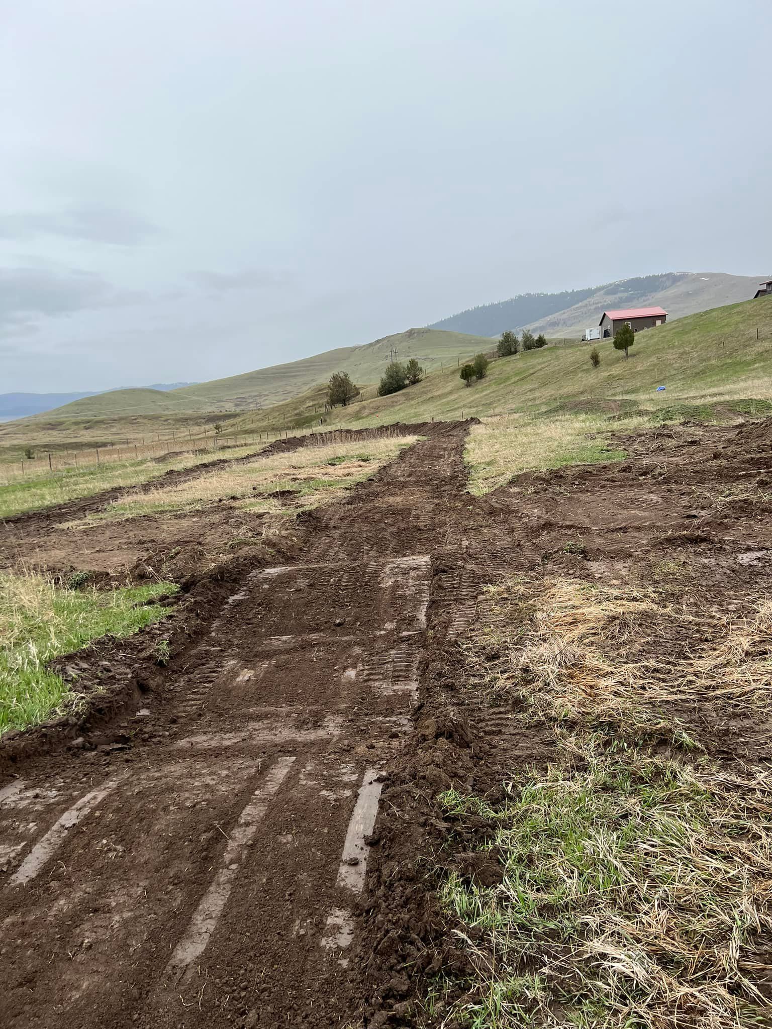A dirt road going through a grassy field with a house in the background.