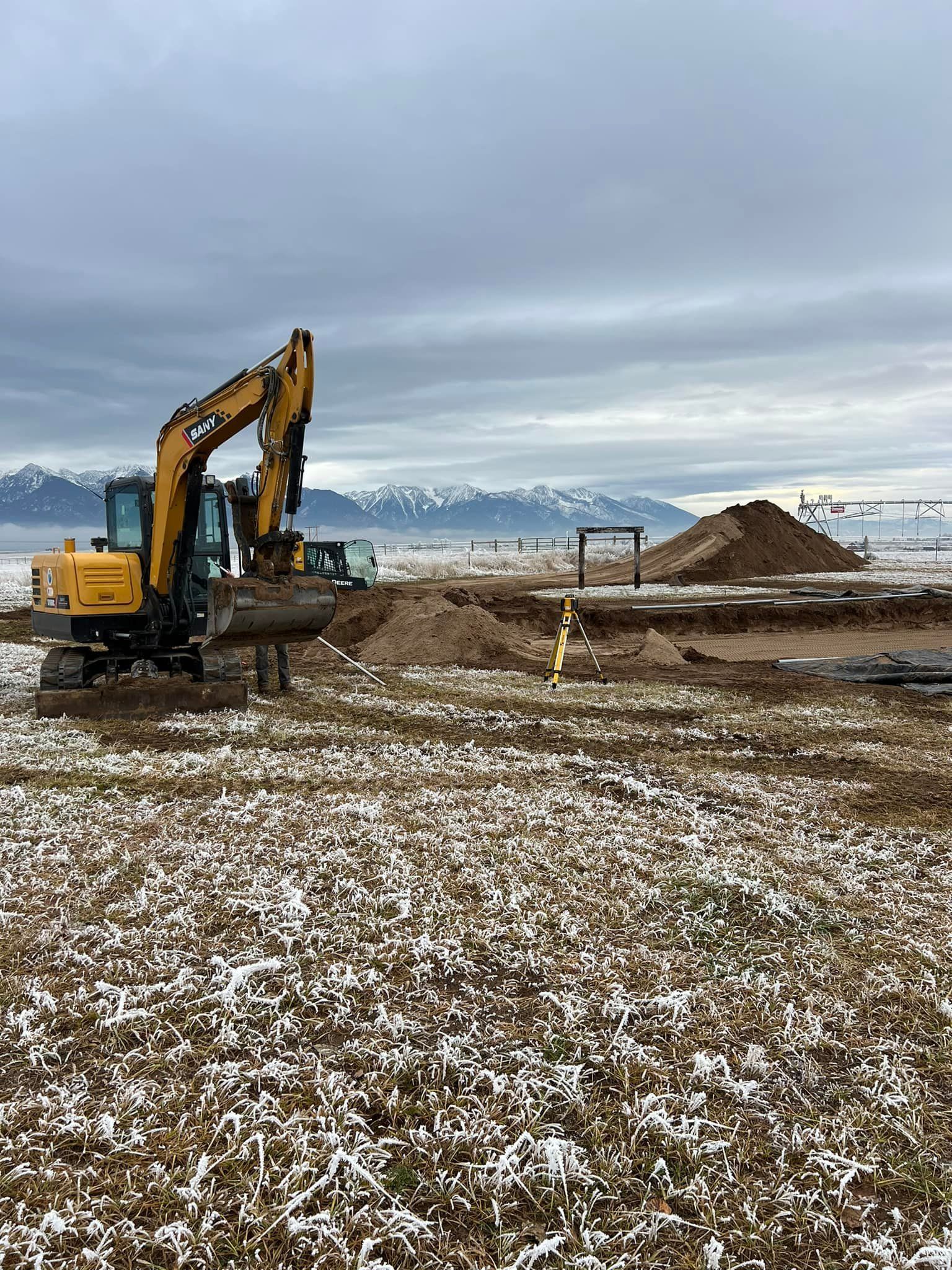 A yellow excavator is working in a snowy field.