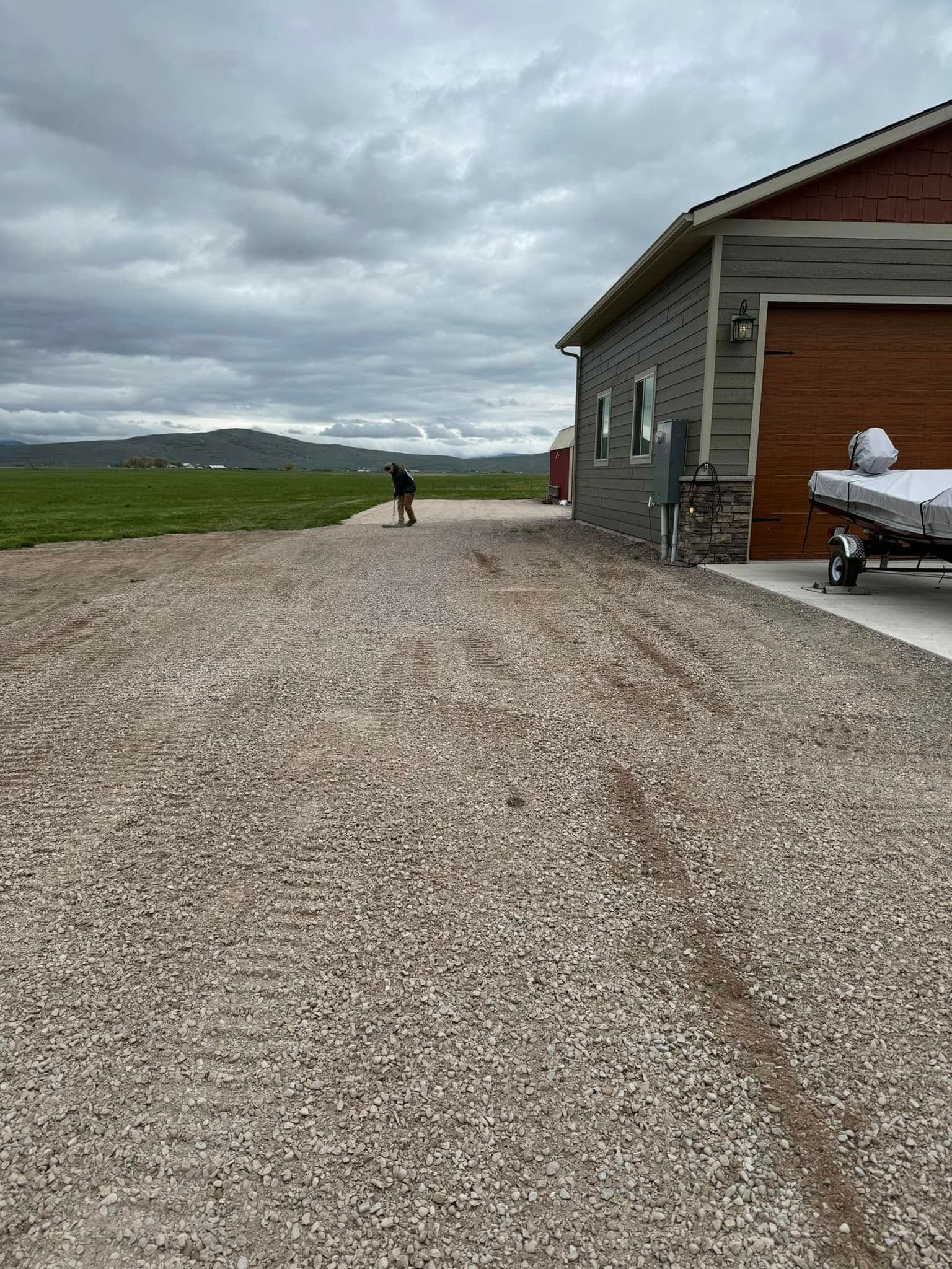 A gravel driveway leading to a house with a boat in the garage.