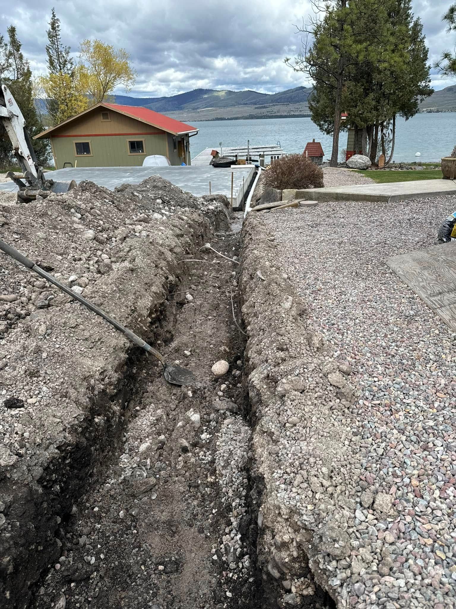 A large hole in the ground next to a lake with a house in the background.