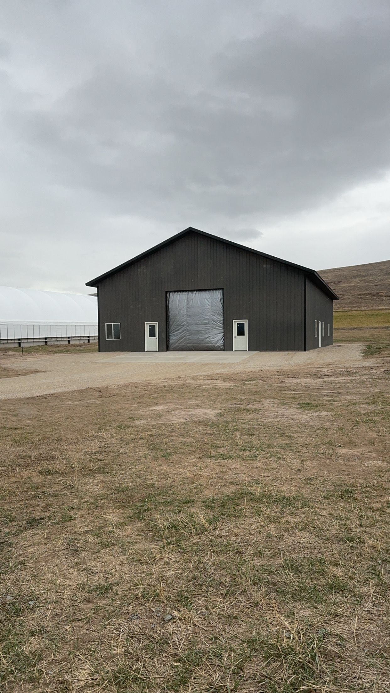 A large black barn is sitting in the middle of a field.