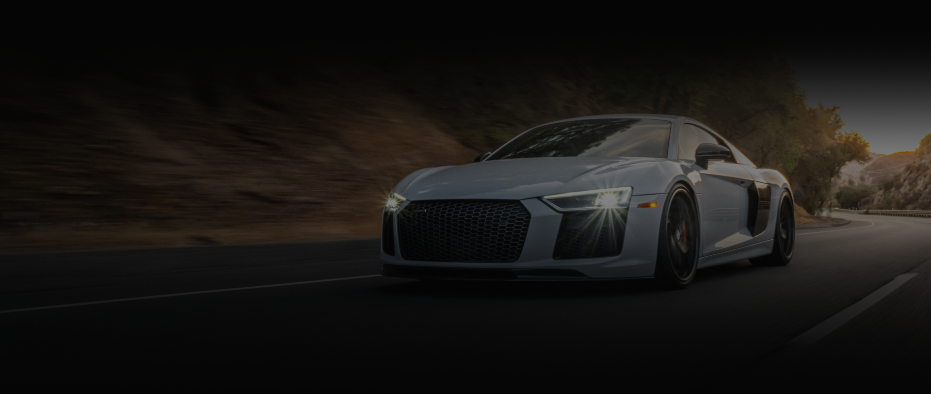 Gray Audi R8 sports car driving on a road with trees and a dark background | Balkan Auto Care