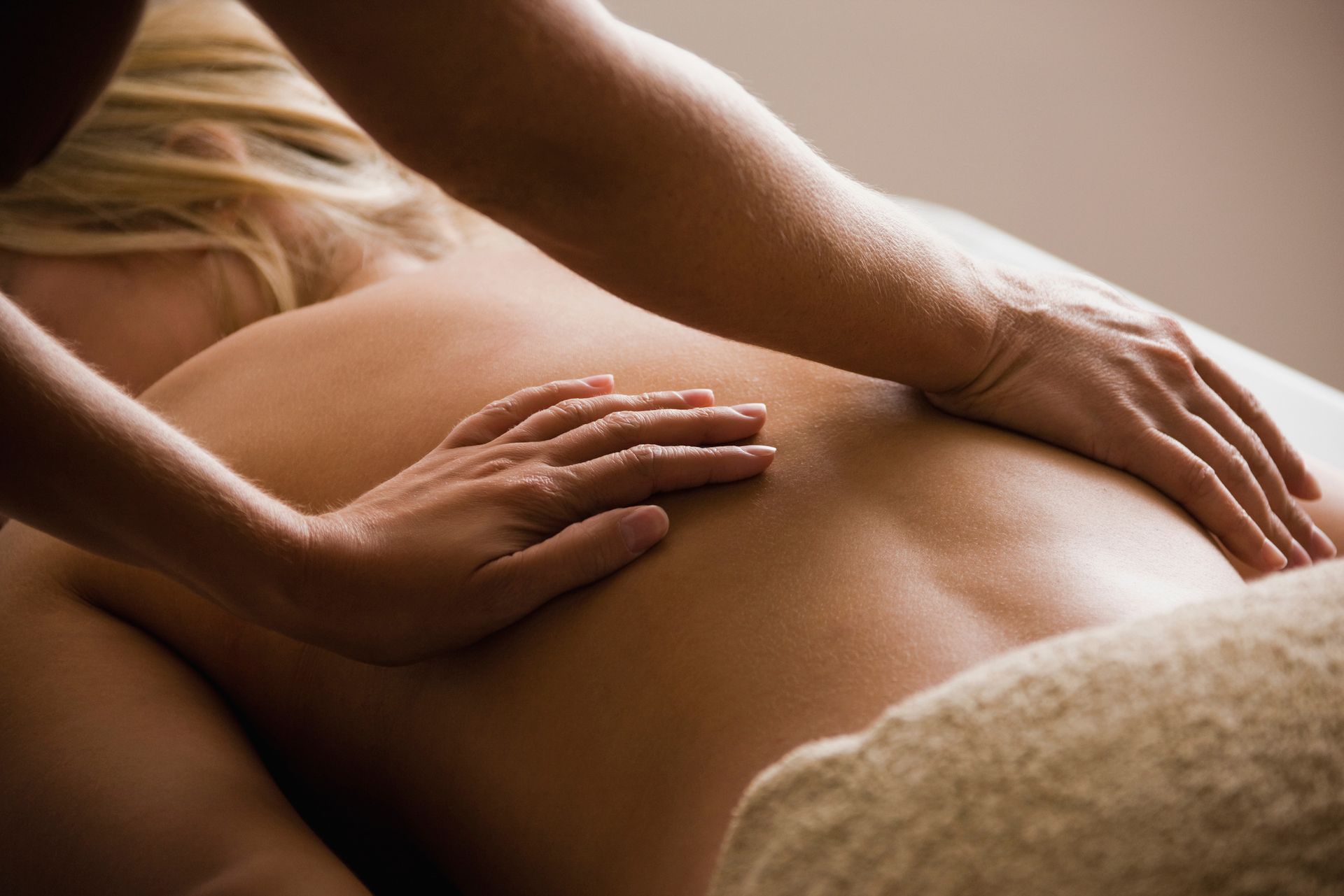 Person receiving a back massage. Hands massaging the back of a woman lying face down on a massage table.