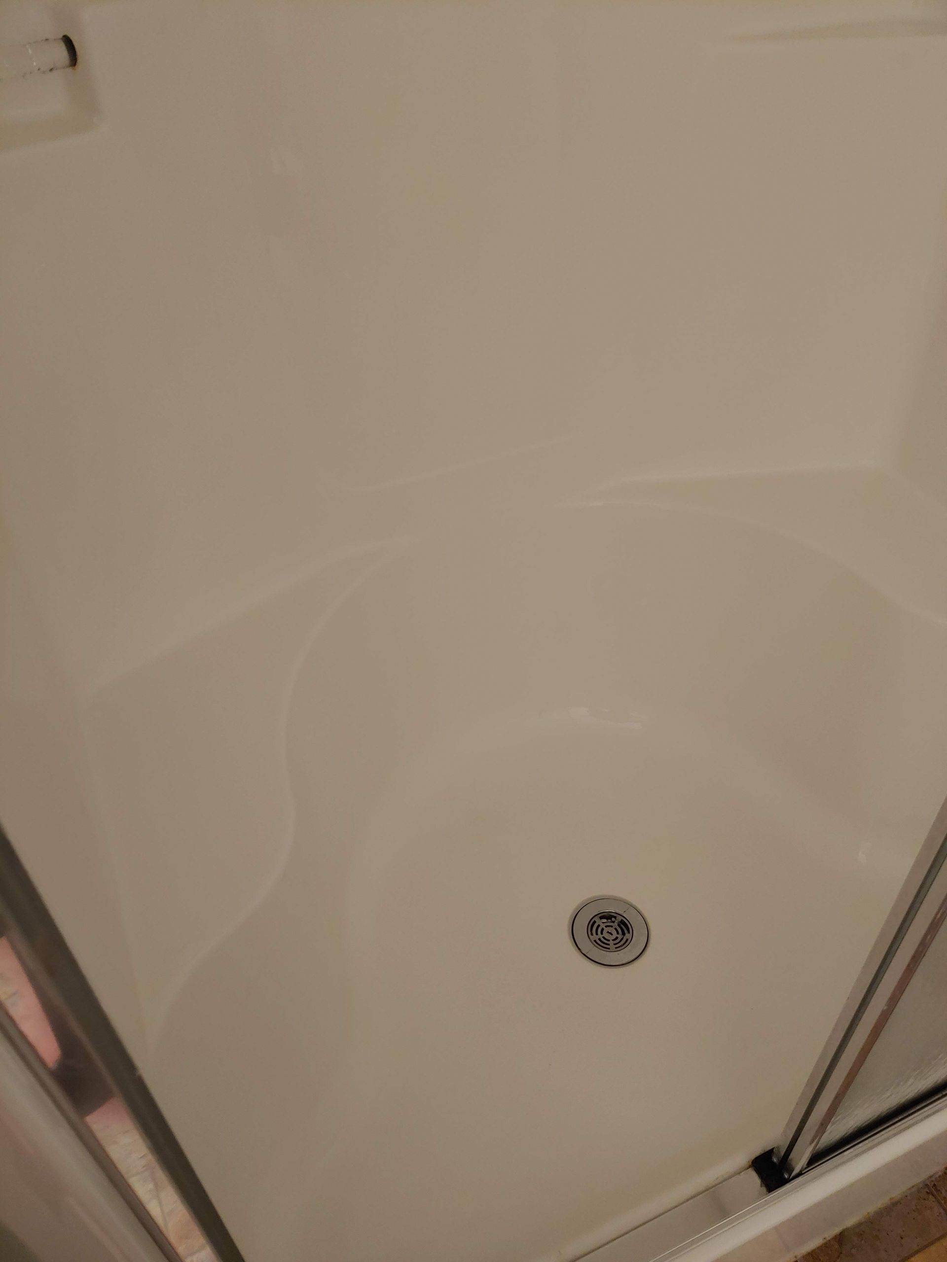 A clean shower stall with a sliding glass door and a drain.