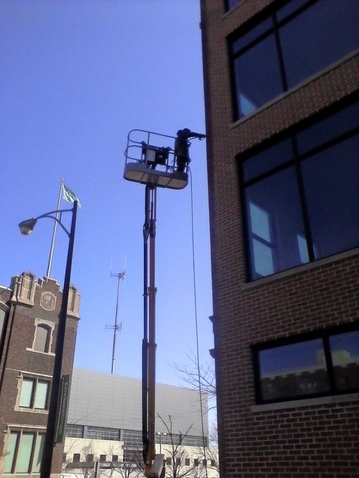 A Man In A Bucket Is Cleaning Windows On A Tall Building — Chicago, IL — McMaster Painting
