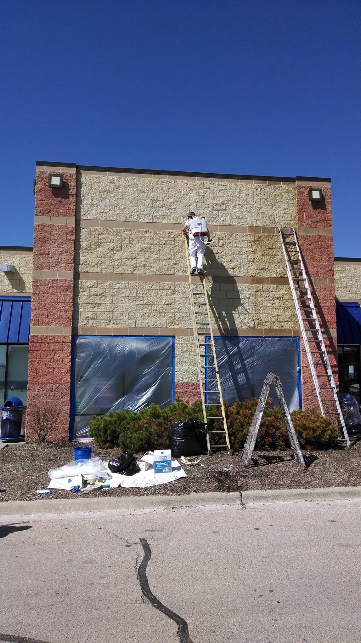 A Man Is Standing On A Ladder Painting The Side Of A Building — Chicago, IL — McMaster Painting