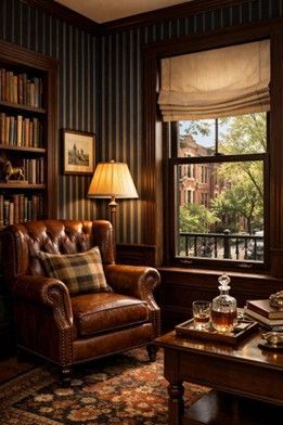 A cozy study with a brown leather armchair, a lamp, a bookshelf, and a window view of trees and buildings.