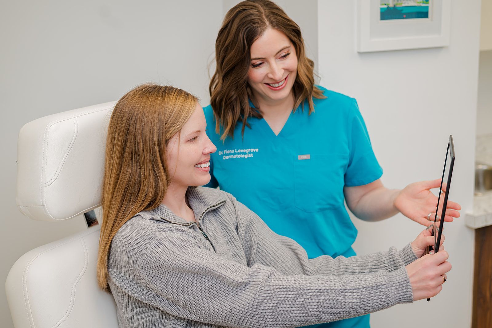 Woman in chair looks at mirror. Dr. Lovegrove in teal scrubs points. Medical setting.
