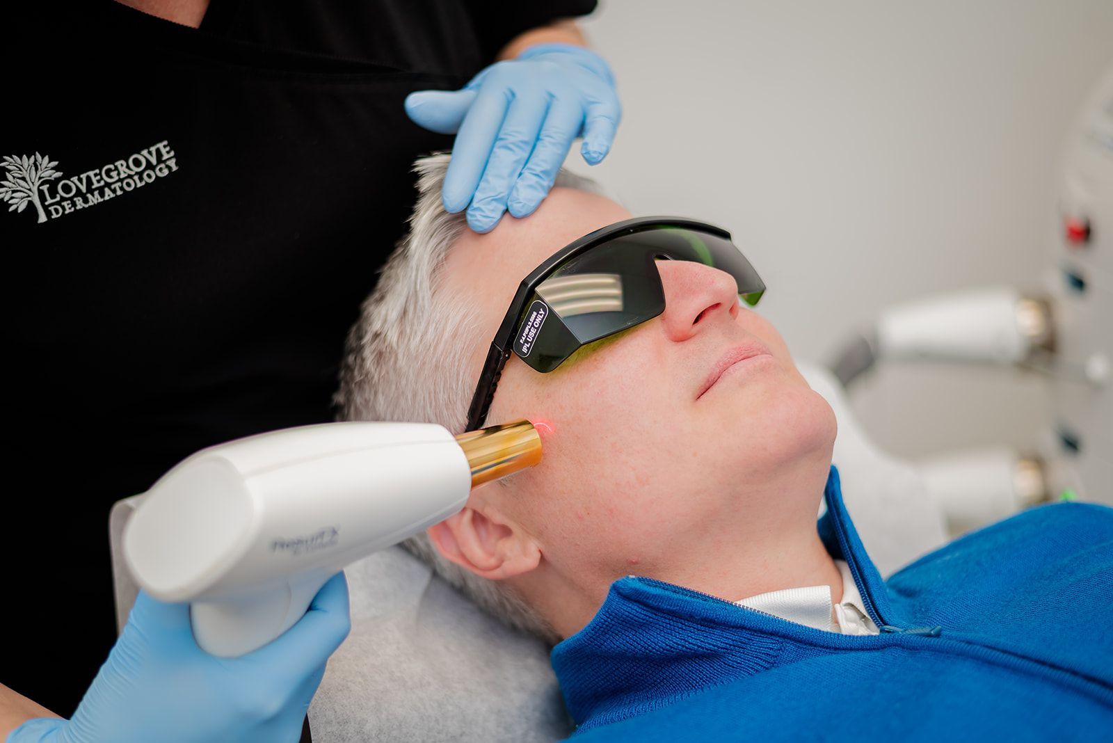 Man receiving laser skin treatment, wearing eye protection, in a medical setting.