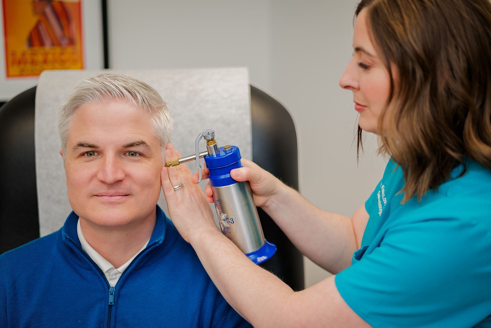 Woman performing cryotherapy on a man's ear in a medical setting. Dr. Lovegrove and patient.