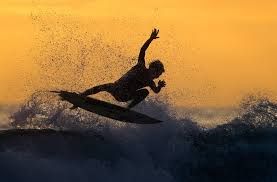 Surfer silhouetted against a golden sunset, mid-air after jumping a wave, water splashing.