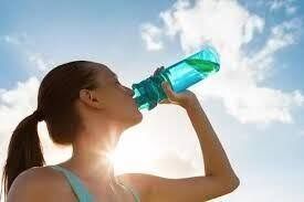 Woman drinking from a blue water bottle outside under a bright blue sky.