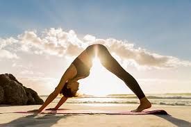 Woman in downward-facing dog yoga pose on beach, sun shining through her body.