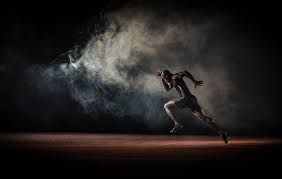 Runner in dark room, body tense, mid-stride, emerging from smoke.
