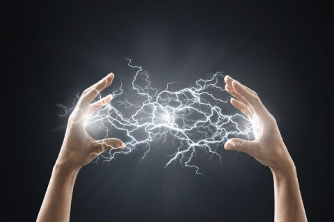 Hands holding and generating bright white electricity against a dark background.