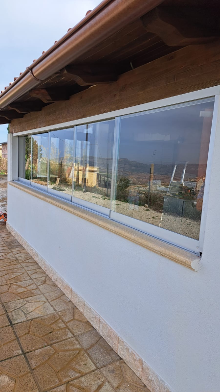 Vista esterna di un edificio con una grande vetrata. Attraverso la finestra si vede il cielo e l'edificio presenta una sporgenza marrone.