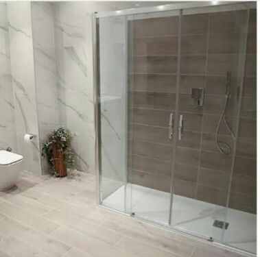 Bagno moderno con doccia in vetro, WC e pareti e pavimento piastrellati in colori chiari.