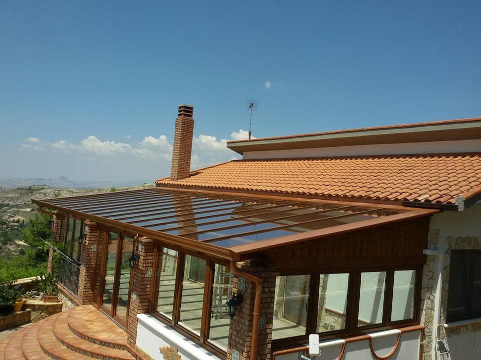 Aggiunta di veranda con tetto in vetro e pilastri in mattoni, annessa a una casa con tetto in tegole, giornata di sole.