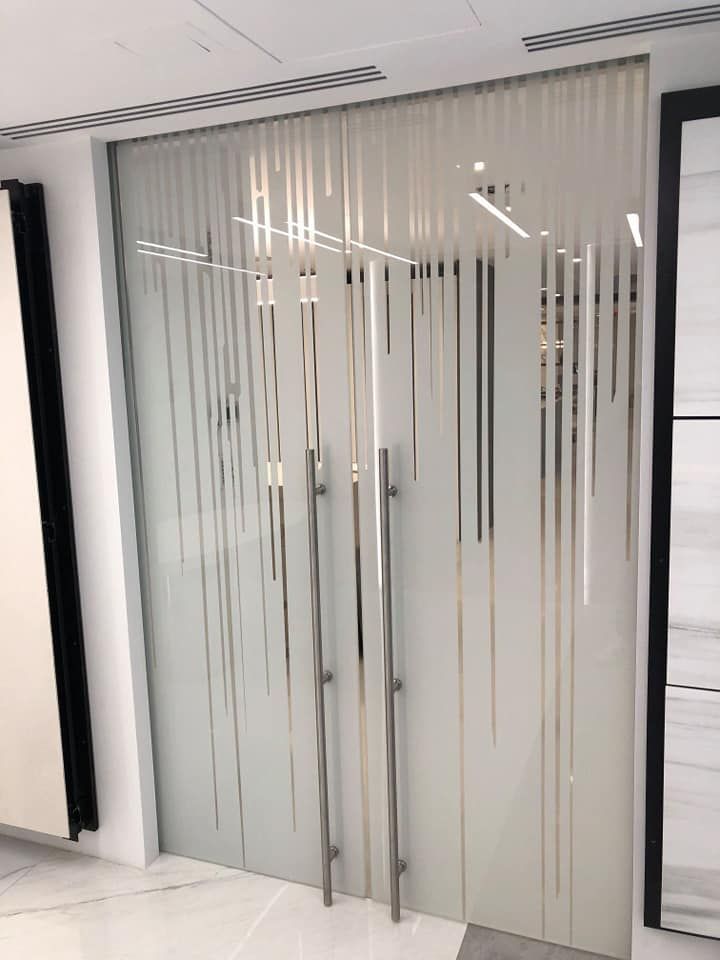Doppie porte in vetro con strisce verticali satinate, maniglie argentate, in uno spazio moderno e luminoso.