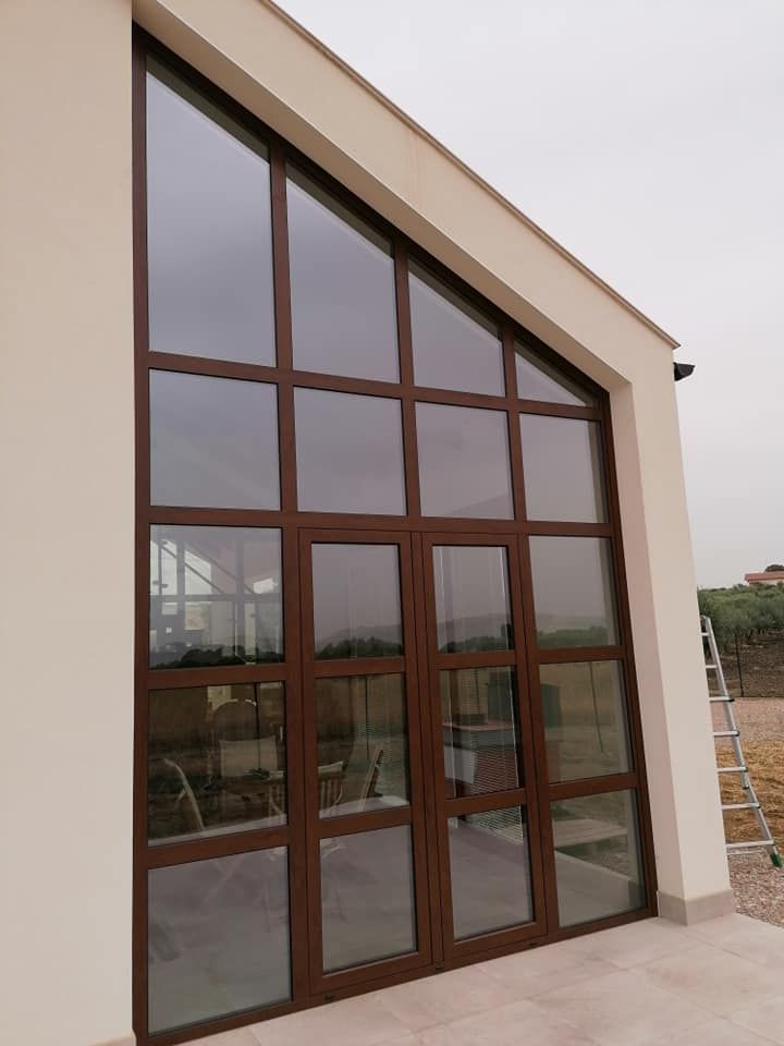 Porte e finestre in vetro con cornice marrone su un edificio bianco, tetto spiovente. Una scala è appoggiata all'edificio.