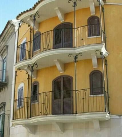 Edificio giallo con due balconi in ferro battuto; persiane marroni e finestre ad arco.