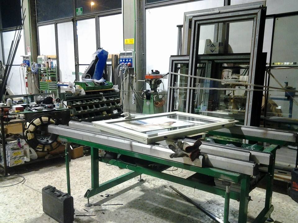 Scena di laboratorio con telai di finestre su un banco da lavoro; utensili e attrezzature visibili.