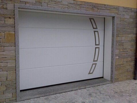 Porta da garage bianca con dettagli grigi curvi, inserita in una cornice in pietra.