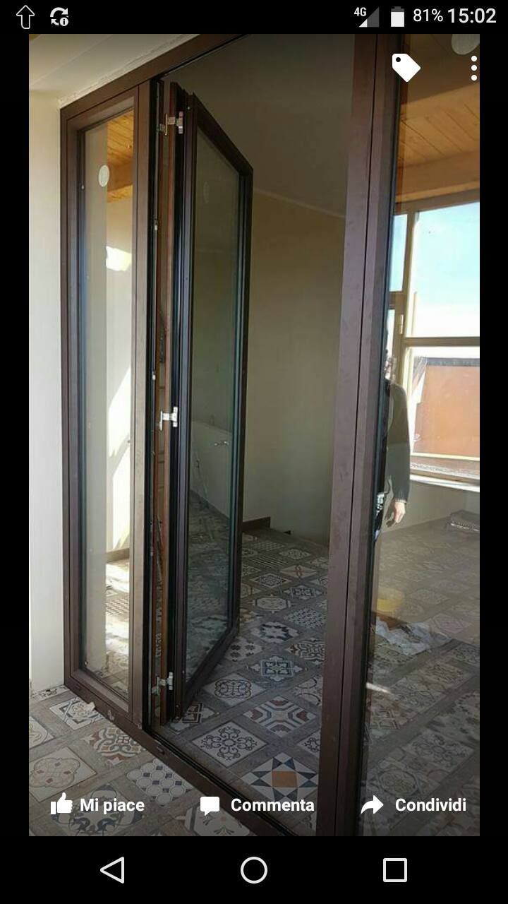 Porta a soffietto in vetro marrone, parzialmente aperta, che rivela un interno piastrellato. Luce solare intensa.