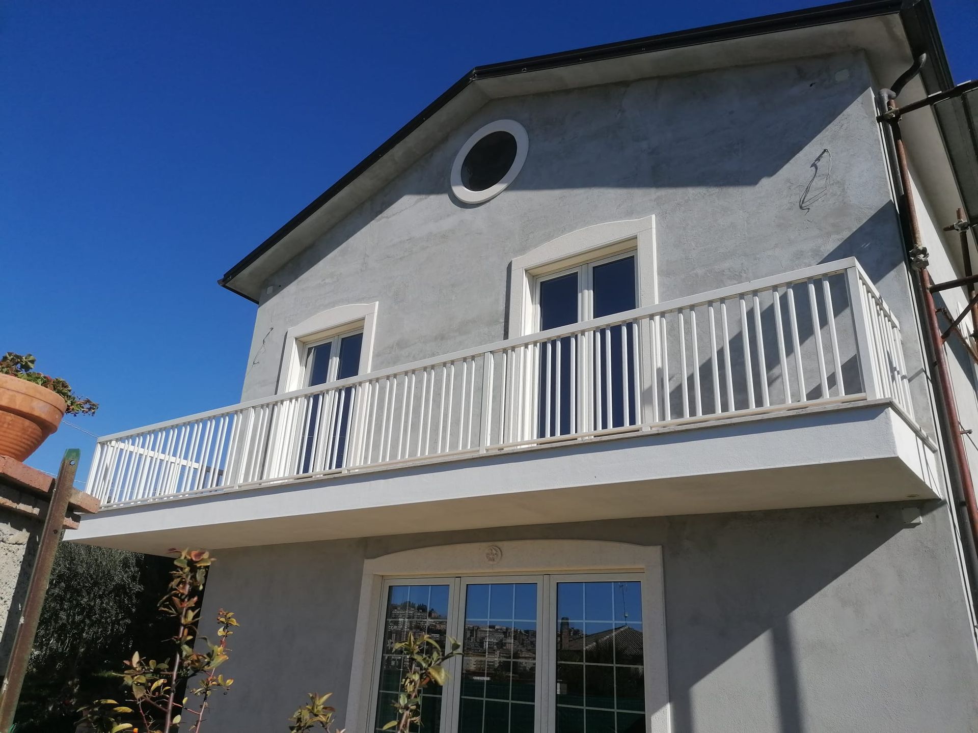Casa grigia a due piani con ringhiera bianca del balcone e finestre sotto un cielo azzurro e terso.