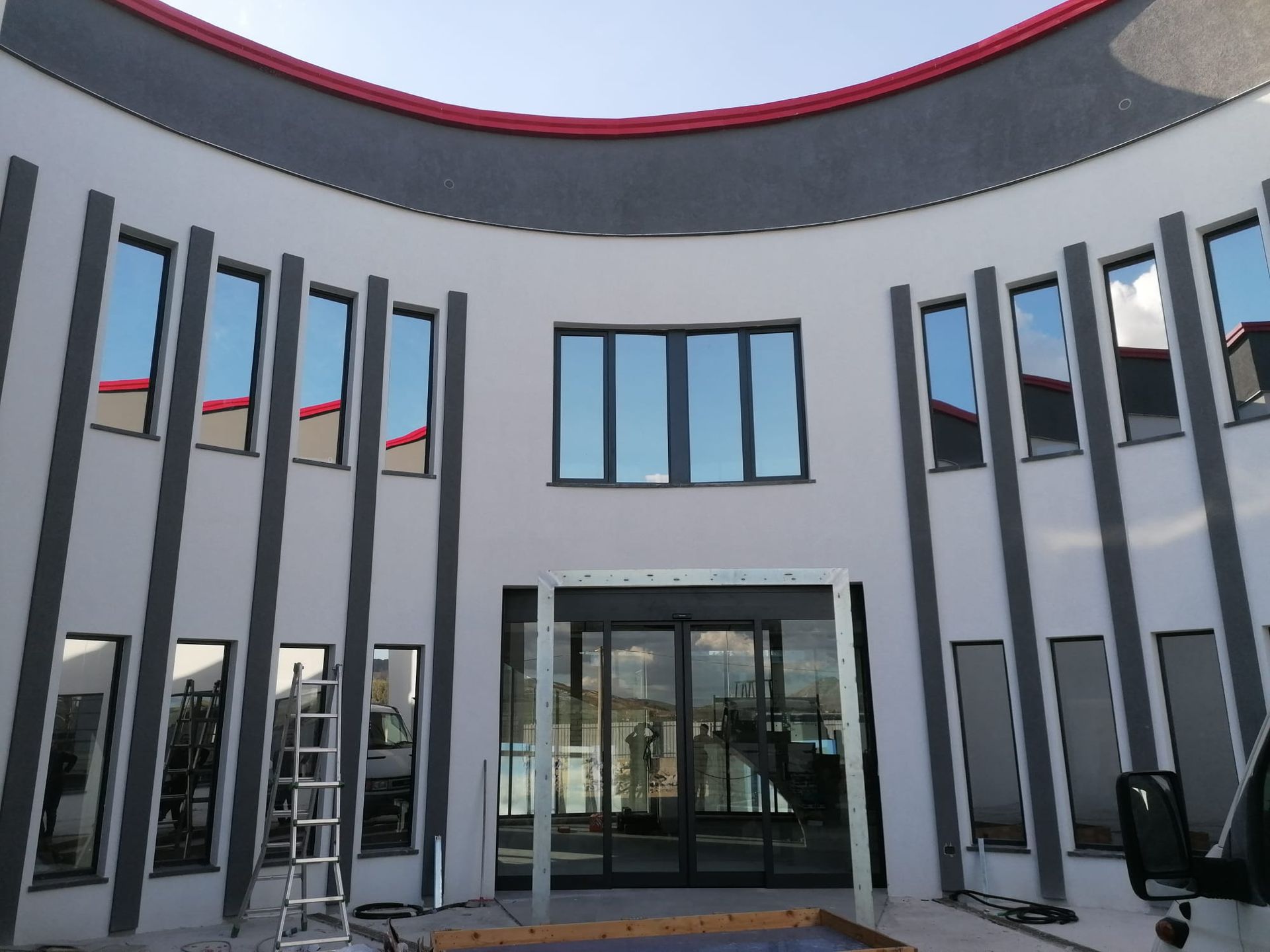 Edificio bianco curvo con numerose finestre, finiture grigie e una fascia rossa in cima.