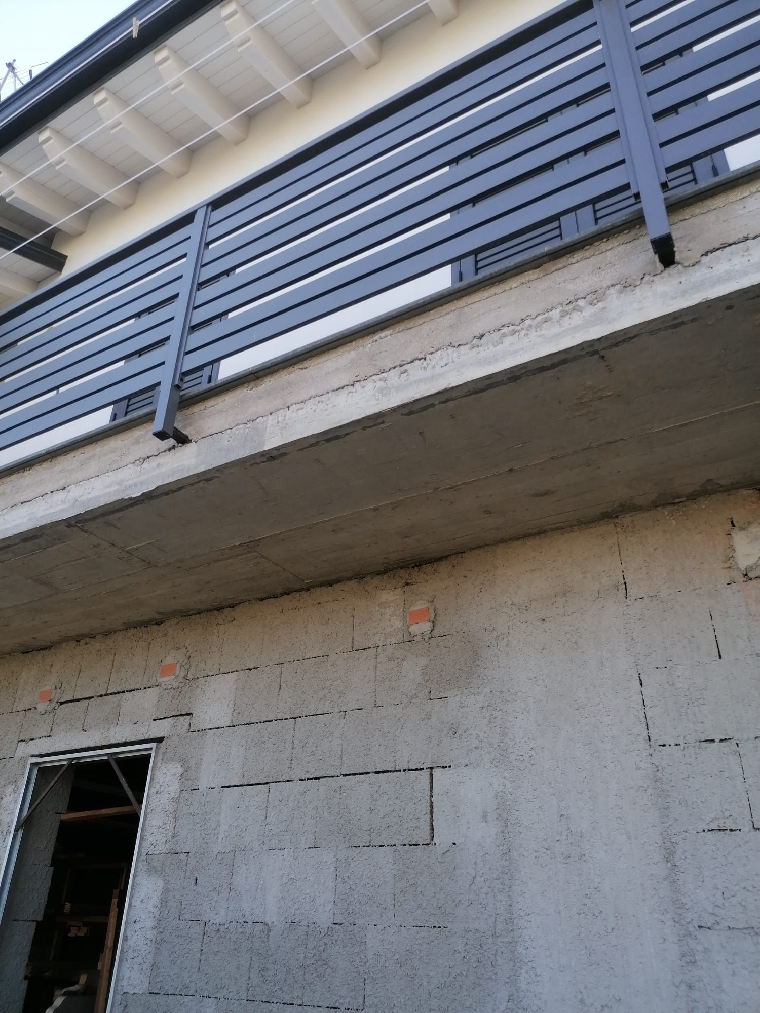 Edificio in cemento grigio con ringhiera in metallo scuro al piano superiore e una porta al piano inferiore.