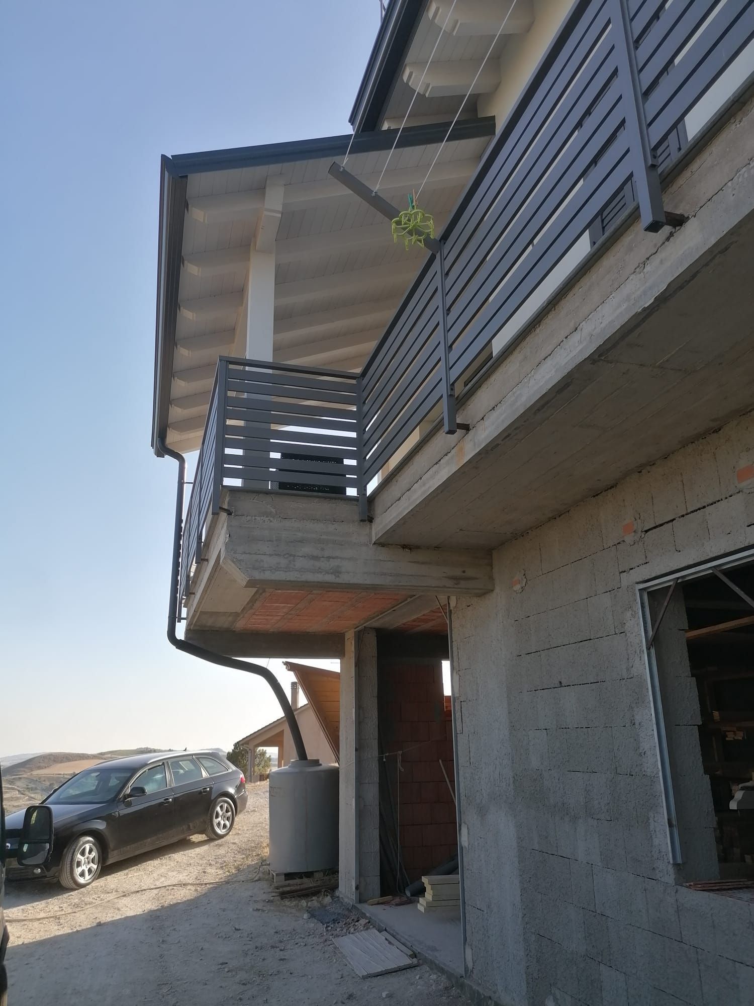 Balcone con ringhiera in metallo grigio su un edificio a due piani. Un'auto è parcheggiata nelle vicinanze.