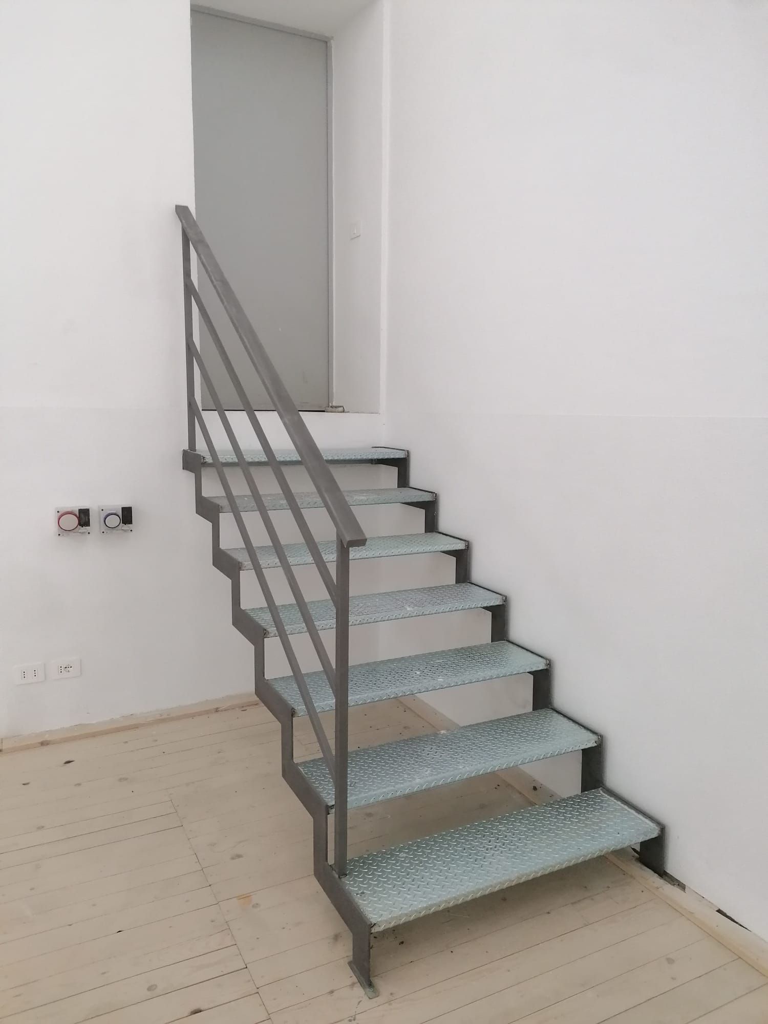 Scala metallica contro un muro bianco, che conduce a una porta.