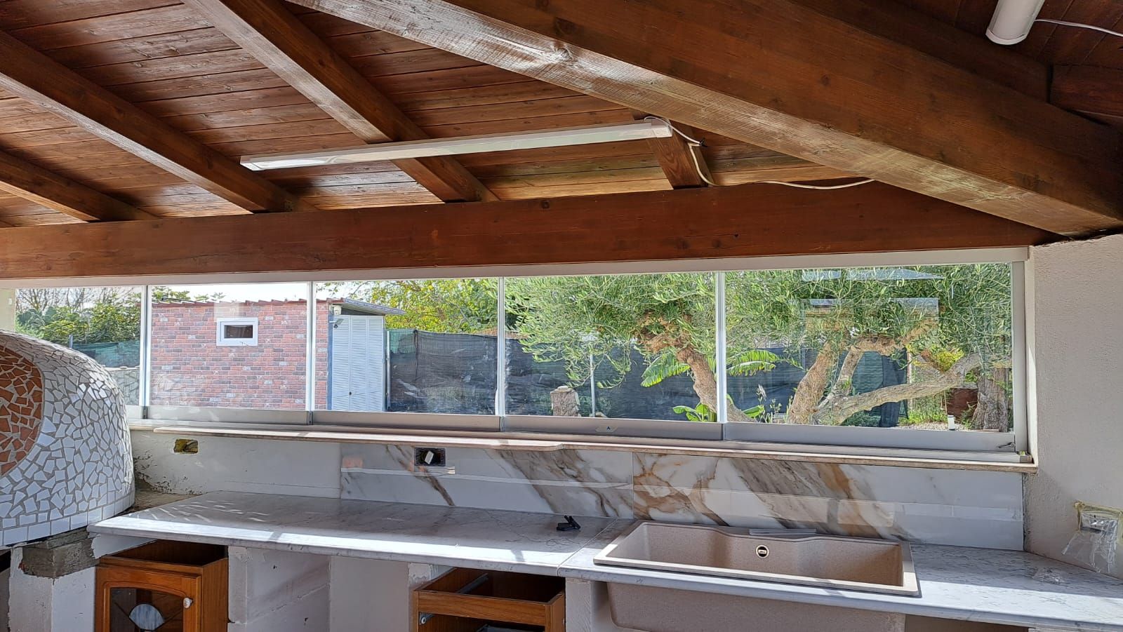 Cucina esterna con ampia finestra con vista sugli alberi e su un edificio in mattoni.