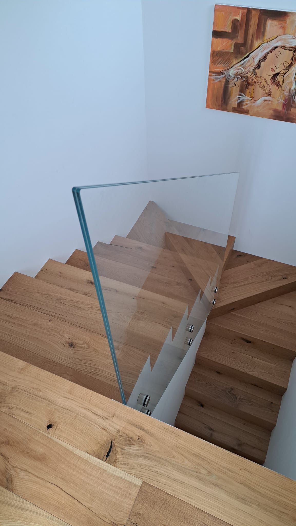 Scala in legno con ringhiera in vetro, pareti bianche. Opera d'arte alla parete.