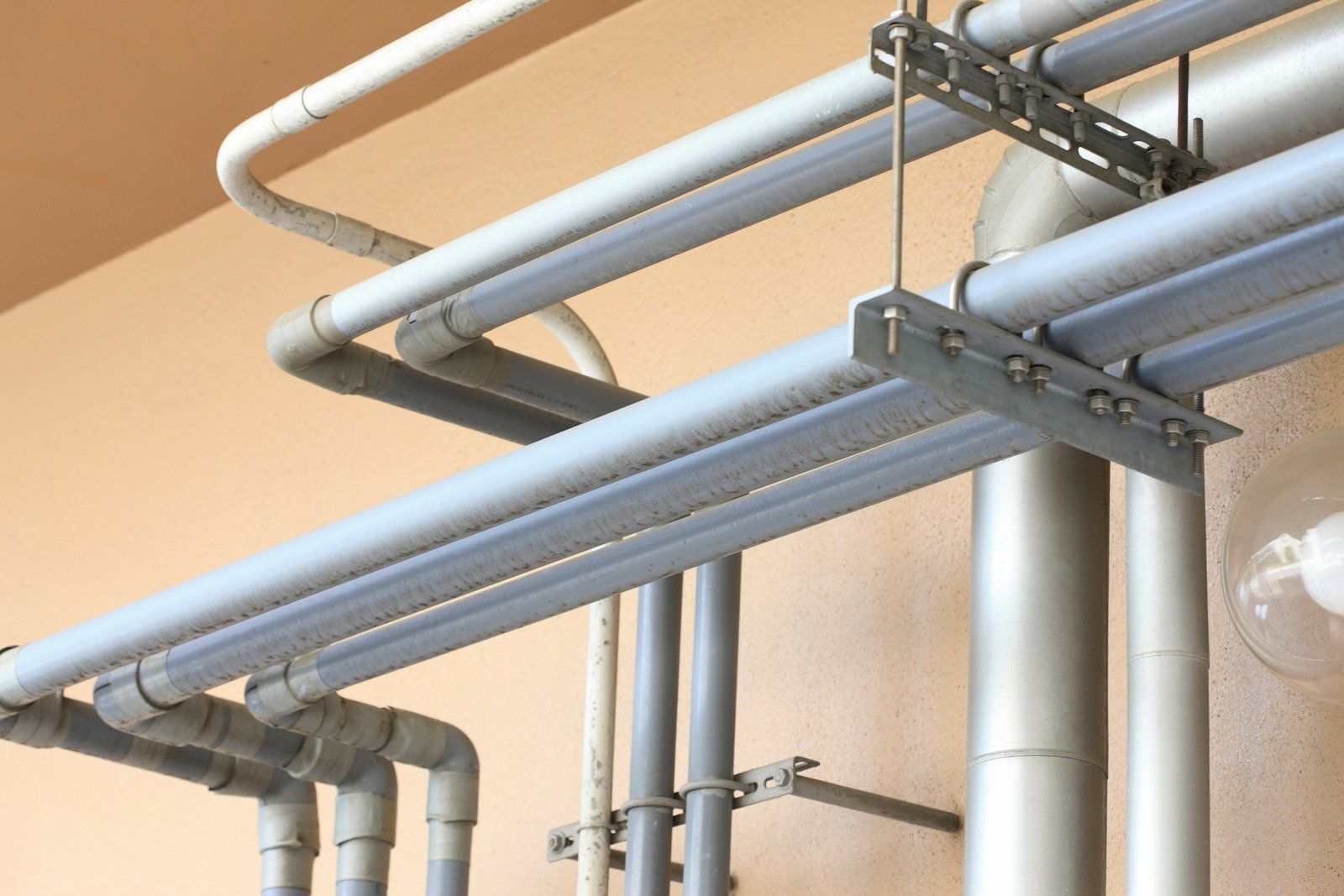 Gray pipes and conduits mounted on a wall, with metal brackets and supports.