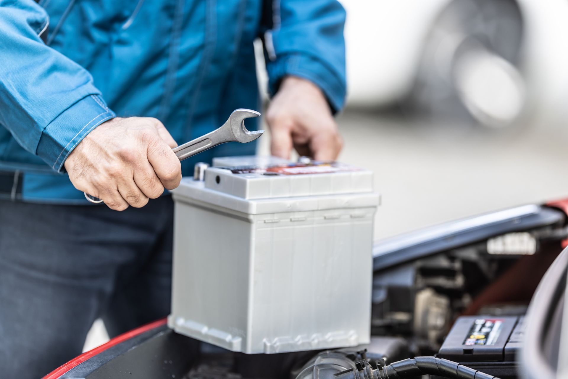 View of a Mechanic Holding a Car Battery and Wrench Over an Open Trunk