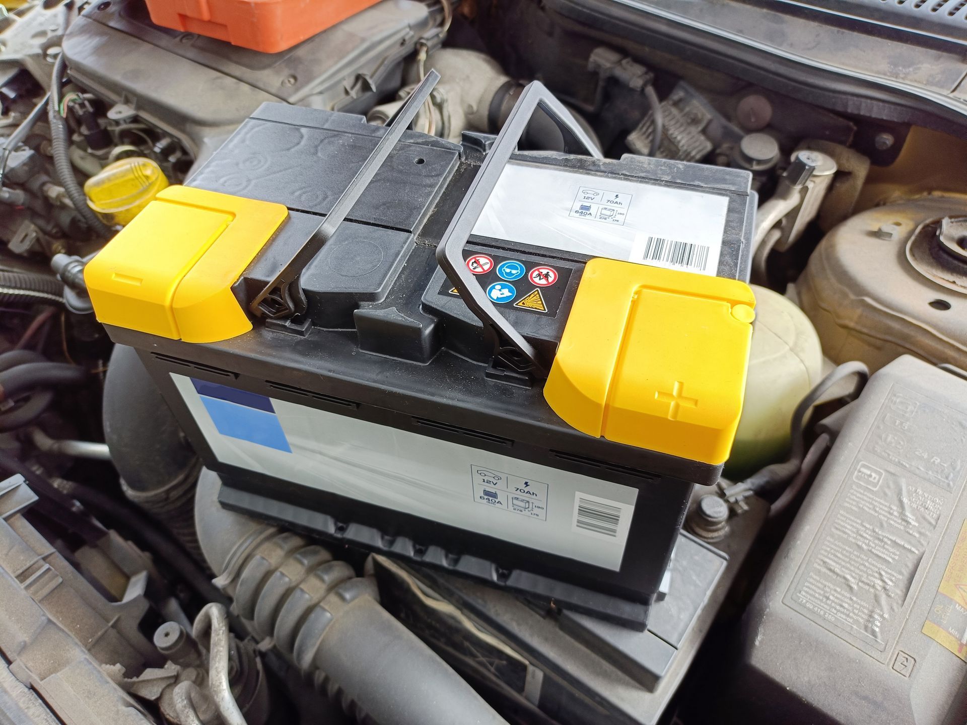 Car battery with yellow terminals installed in an engine bay.