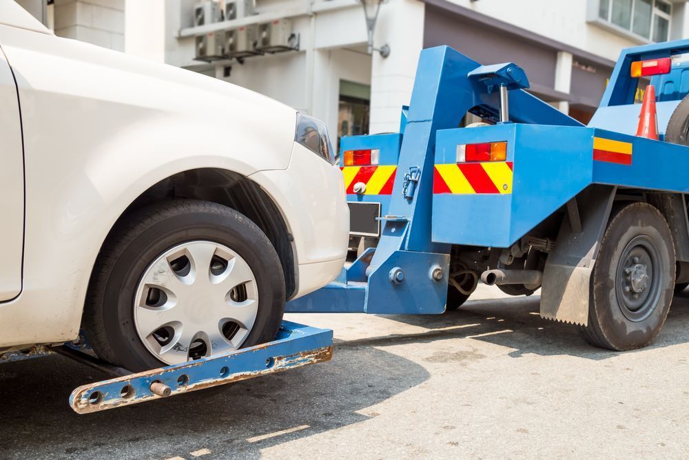 A White Car Is Being Towed By A Blue Tow Truck — Big Tim's Towing in Rutherford, NSW