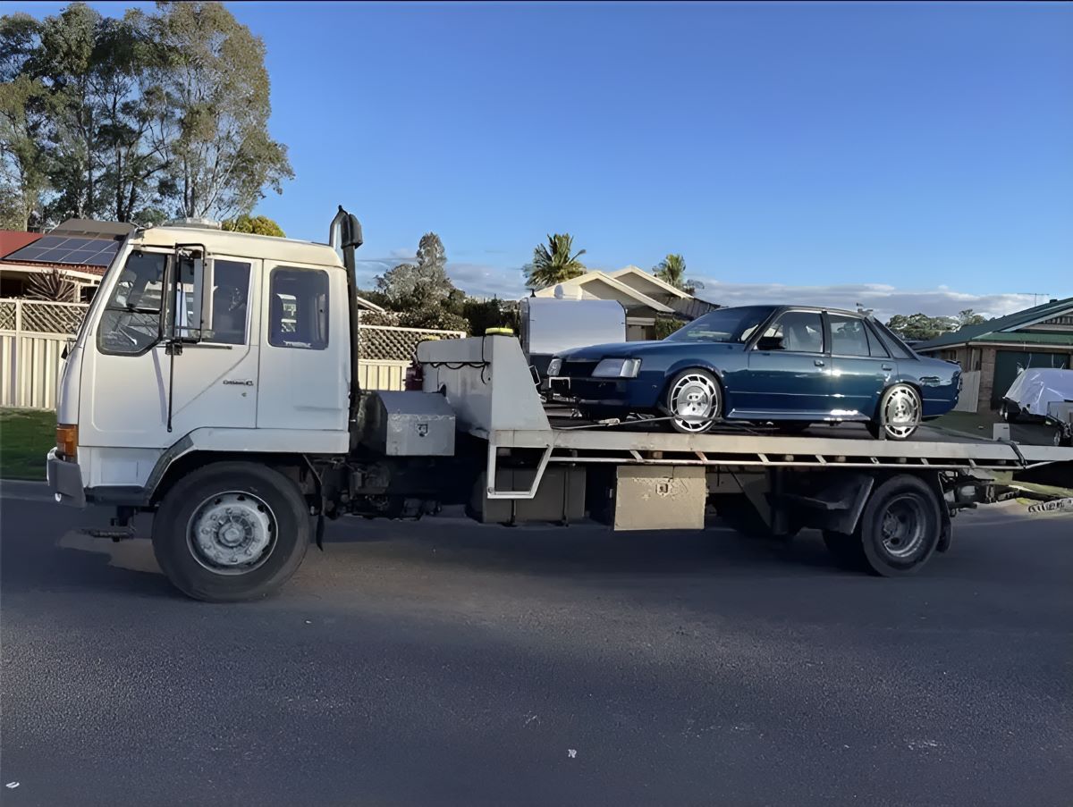 A Tow Truck, Carrying A Blue Car On Its Back, Is Parked By The Roadside — Big Tim's Towing in Charlestown, NSW