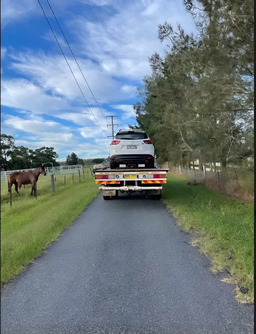 A Car Is Being Towed Down A Country Road By A Tow Truck — Big Tim's Towing in Bennetts Green, NSW