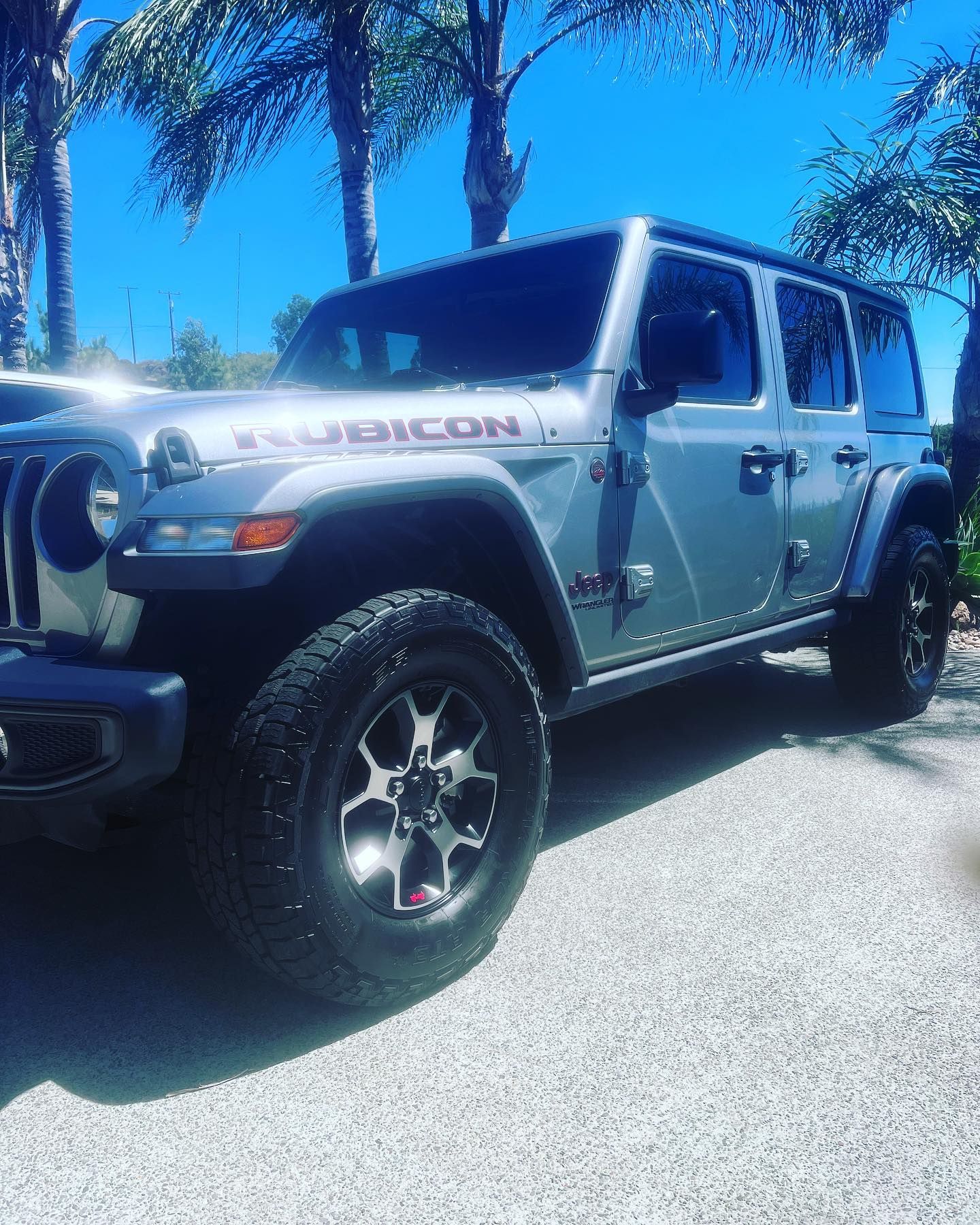 A silver jeep with the word rubicon on the side is parked in a parking lot.