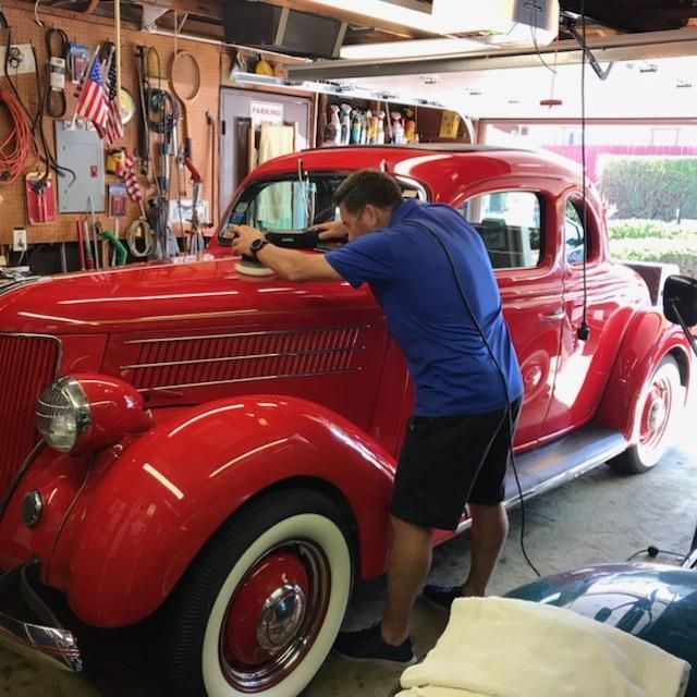 A man in a blue shirt is polishing a red car