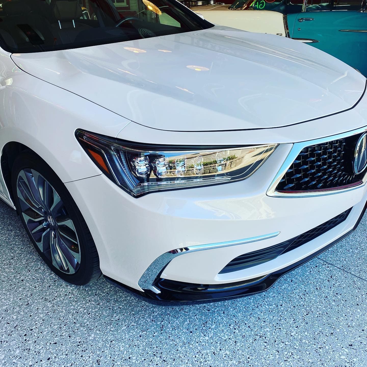 A white car is parked in a garage with a blue car in the background.