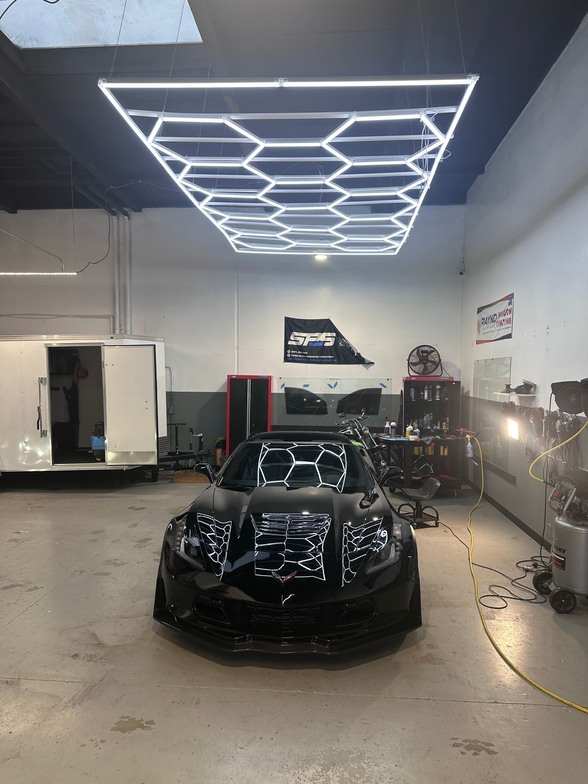 A black car is parked in a garage under a honeycomb light.